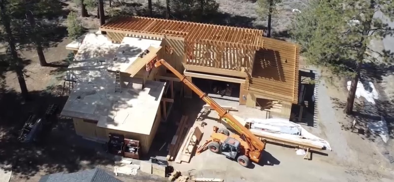 Aerial drone view of custom home under construction crane and timber framing Truckee CA