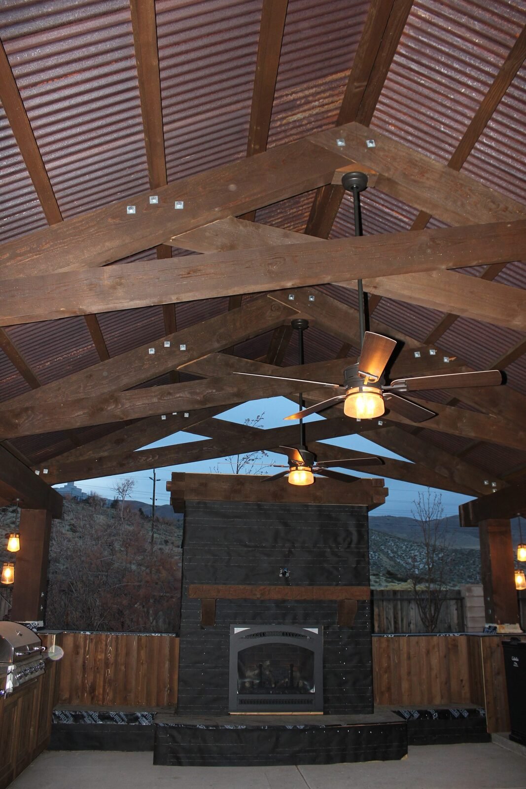 Finished covered outdoor kitchen timber frame fireplace ceiling fans pendant lights at dusk Reno NV